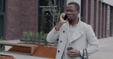Afro-Amerikalı işadamı cep telefonuyla konuşuyor ve kahve içmeye gidiyor. Profesyonel iletişim ve kentsel yaşam tarzı kavramı.