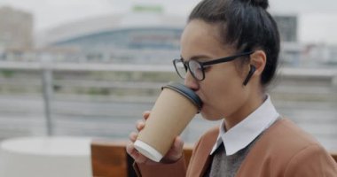 İş kadınının eğik portresi kahve içerken kablosuz kulaklıkla müzik dinlerken ve sokakta dizüstü bilgisayar kullanırken. Modern yaşam tarzı ve iş insanları kavramı.