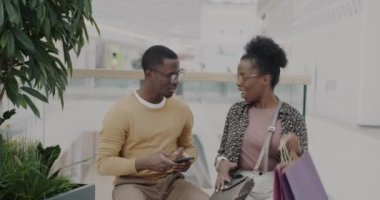 Genç Afrikalı Amerikalı bir kadın, elinde kese kağıtlarıyla yeni mallar gösterip alışveriş merkezinde eğleniyor. İlişki ve perakende kavramı.