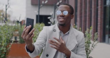 Başarılı bir Afro-Amerikan işadamı, akıllı telefonuyla çevrimiçi video görüşmesi yapıyor ve şehir sokaklarında açık hava ekranlarına bakıyor. İş iletişimi ve mesleki sohbet kavramı.