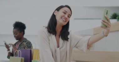 Neşeli genç bayan video konuşması yapıyor ve alışveriş merkezinde akıllı telefon kullanarak el sallıyor. Perakende ve iletişim konsepti.