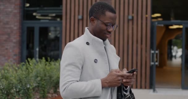 美国黑人商人站在市中心的写字楼外 用智能手机发短信的肖像 商业和小玩艺儿概念 — 图库视频影像