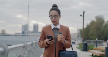 Orta Doğulu bir kadının kahve içmek için elinde akıllı telefon tutarak şehirde yürüdüğü bir fotoğraf. Başarılı iş adamı ve şehir yaşam tarzı konsepti.