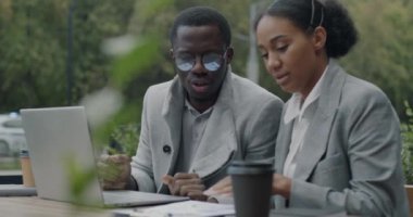 Afro-Amerikan iş ortakları şehir caddesindeki açık hava kafede dizüstü bilgisayarla konuşuyor ve çalışıyor. Modern teknoloji ve takım çalışması kavramı.