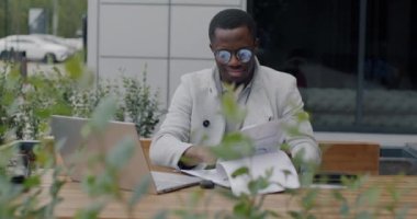 Afro-Amerikalı girişimci iş belgelerini okuyor kahve içiyor ve şehirdeki bir kafede dizüstü bilgisayar kullanıyor. Profesyonel meslek ve başarılı insanlar konsepti.