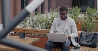 İş adamı dışarıda oturuyor ve profesyonel aktivitelere odaklanmış bir şekilde dizüstü bilgisayarla çalışıyor. Modern teknoloji ve girişimciler konsepti.