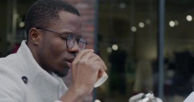 Afrika kökenli Amerikalı iş adamının kahve içmesi ve sokak kafesinde finansal belgelerle çalışması. Halk ve şehir yaşam tarzı kavramı.