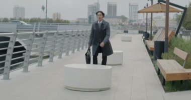 Neşeli Asyalı girişimci yavaş hareket ederek şehir caddesinde evrak çantasıyla zıplıyor. Neşeli iş adamı ve olumlu duygu konsepti.