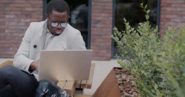 Başarılı bir Afro-Amerikan işadamı, şehir sokaklarında online olarak çalışan dizüstü bilgisayarlı daktilo kullanıyor. Modern teknoloji ve iş kavramı.