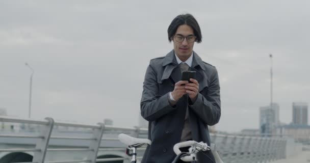 アジアのビジネスマンがスマートフォンでテキストを送り 自転車を持っている屋外のソーシャルメディアでチャットを楽しんで笑います コミュニケーションとガジェットのコンセプト — ストック動画