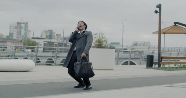 アジアのビジネスマンが携帯電話で話し 街の外で幸せを表現するダンスを楽しみました 勝利と事業実績コンセプト — ストック動画