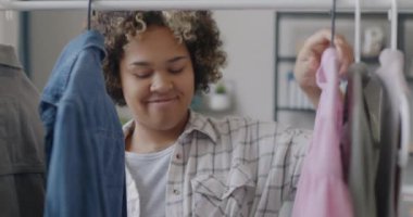 Gülümseyen Afro-Amerikalı kadın, evdeki kıyafetlere bakarak demiryolu askısına şık giysiler asıyor. Moda ve evcil rutin kavram.