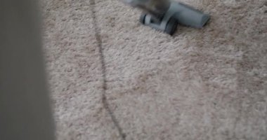 Modern elektrik süpürgesinin yakın çekim görüntüsü yumuşak halıda hareket ediyor yerleri süpürüyor ve kimse görünmüyor. Ev aletleri ve teknoloji konsepti.