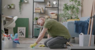 Yorgun, genç bir adam ev sahibi. Yerleri bez ve deterjanla yıkıyor. Yorgun ve yorgun hissetmeye çalışıyor. Ev işleri ve ev işleri konsepti.