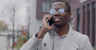 Kendine güvenen Afrikalı Amerikalı girişimci cep telefonuyla konuşuyor. Açık havada iş konuşuyorlar. Profesyonel iletişim ve iş konuşması kavramı.