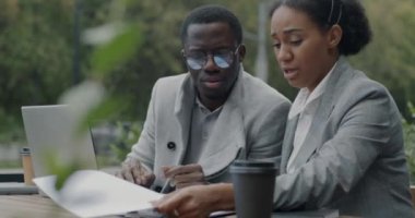 Diz üstü bilgisayar kullanan ve şehir dışındaki kafede iş belgeleriyle çalışan Afro-Amerikalı erkek ve kadın girişimciler. Başarılı takım çalışması ve modern teknoloji konsepti.