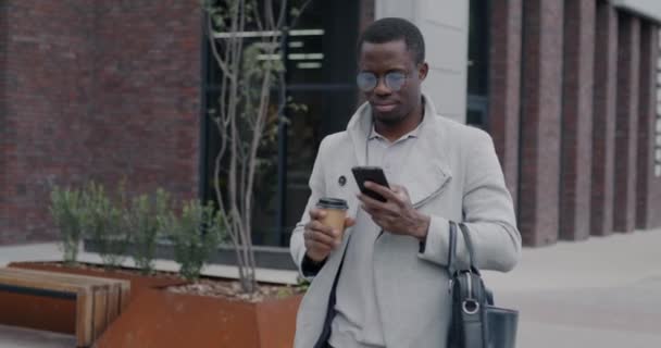 African American Businessman Walking City Street Using Smartphone Drinking Coffee — Stock Video
