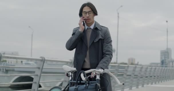 Kaygısız Asyalı Işadamı Şehir Merkezinde Elinde Bisikletle Cep Telefonuyla Konuşuyor — Stok video