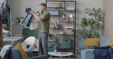 Kirli çamaşırları toplayan genç bir adam dağınık bir apartman dairesinde temizlik yapıyor evde çamaşır yıkıyor. Modern yaşam tarzı ve ev işleri kavramı.
