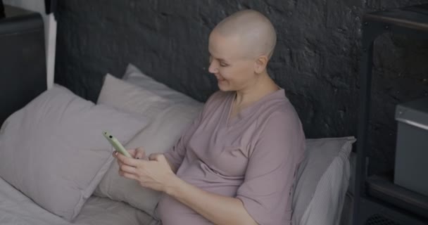 スマートフォンのメッセージングを使用して楽しい妊婦と自宅でベッドでリラックスして笑う 現代の技術と幸せな妊娠のコンセプト — ストック動画