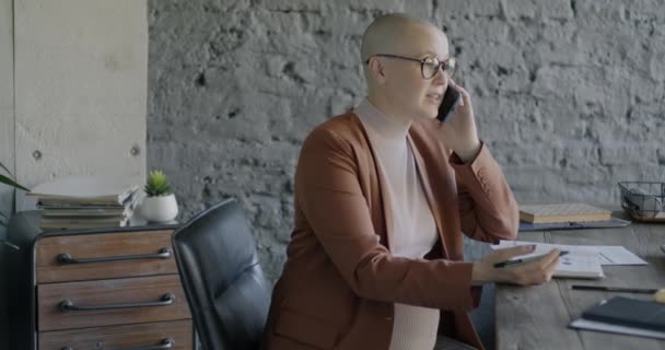 妊娠中のビジネス女性は 現代のオフィスでデスクに座っている作業を議論する携帯電話で話しています 妊娠とプロの職業コンセプト — ストック動画