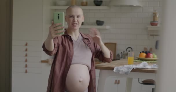 アパートのキッチンに立っているスマートフォンを使って 母親が話して手を振ることを期待しています コミュニケーションと妊娠のコンセプト — ストック動画