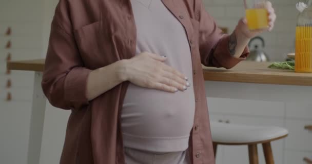 アパートのキッチンに立っているオレンジジュースを飲むかわいい妊婦のスローモーションティルトアップ肖像画 妊娠と健康的なライフスタイルの概念 — ストック動画