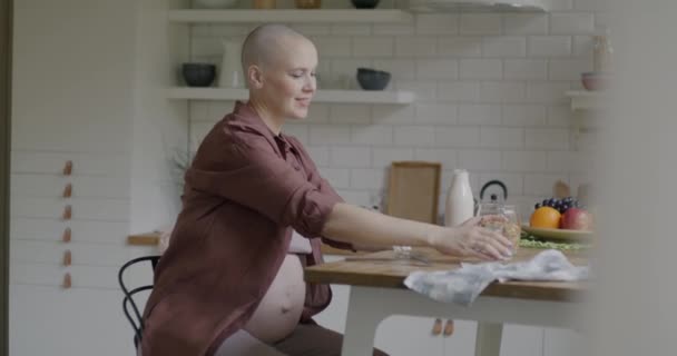 妊娠中の若い女性が自宅のキッチンで食卓に座って健康的な朝食を食べるスローモーション 栄養と妊娠のコンセプト — ストック動画