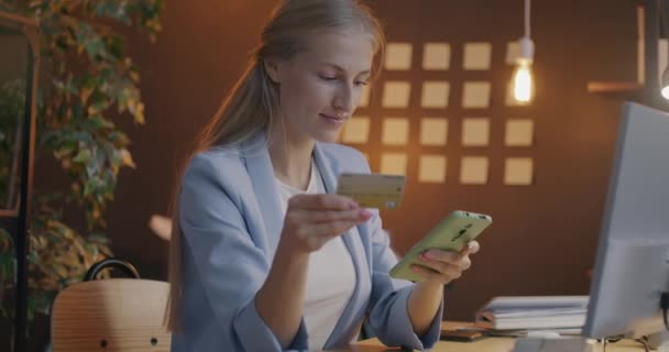 スマートフォン保有のクレジットカードで 夜間にオフィスで無線送金を楽しんで笑顔で幸せな女性起業家のスローモーション ファイナンスとビジネスコンセプト — ストック動画