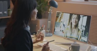 Genç iş kadınları online video görüşmeleri sırasında geceleri ofislerindeki bilgisayarı kullanarak konuşuyor. İş birliği ve modern teknoloji kavramı.