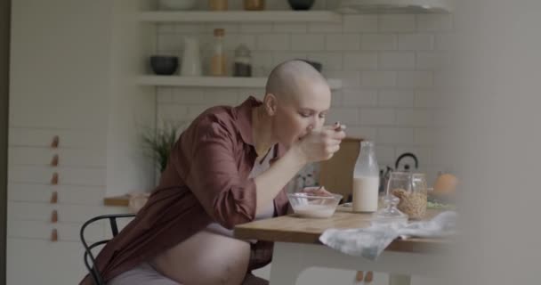 現代の家でキッチンで健康的な朝食ミューズリーとミルクを食べる美しい妊婦の将来の母親のスローモーション 妊娠と栄養に関するコンセプト — ストック動画