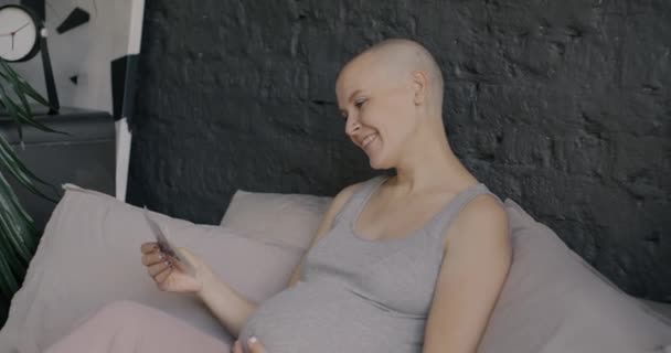 自宅でベッドでリラックスした写真を楽しんで笑顔の赤ちゃんのソノグラム画像を見ている未来の母親のゆっくりとした動き 妊娠と家族の概念 — ストック動画