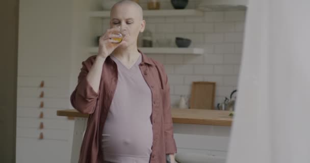 母親がオレンジジュースを飲んで 自宅のキッチンで妊娠を楽しんでいる腹の笑顔に触れることを期待している幸せな女性 健康的なライフスタイルと計画家族のコンセプト — ストック動画