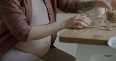 Hamile bir kadının kahvaltılık gevrek yiyip evde sağlıklı yemeğin tadını çıkardığı yakın plan. Hamilelik ve beslenme konsepti.