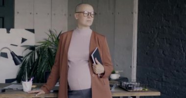 Ofiste kameraya dönen hamile bir kadının yavaş çekim portresi. Mesleki meslek ve hamilelik kavramı.