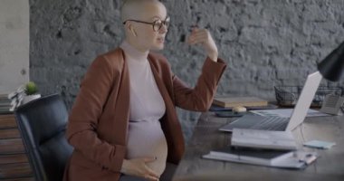 Hamile iş kadını internette bilgisayar ve kablosuz kulaklıkla telefonla konuşuyor. İletişim ve iş konsepti.
