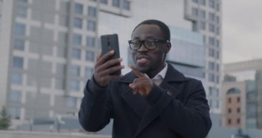 İhtiraslı Afrikalı Amerikalı yönetici şehir sokaklarında akıllı telefonları kullanarak online video görüşmeleri sırasında konuşuyor. Sanal toplantı ve iletişim konsepti.