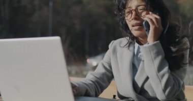 Orta Doğulu iş kadını dizüstü bilgisayar kullanıyor ve cep telefonuyla konuşuyor. Şehir merkezindeki kafede çalışıyor. İş iletişimi ve modern teknoloji kavramı.