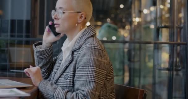 忙しい女性起業家は 携帯電話で話し カフェのテーブルに座っているラップトップコンピュータでタイプします プロフェッショナルなコミュニケーションと人々のコンセプト — ストック動画