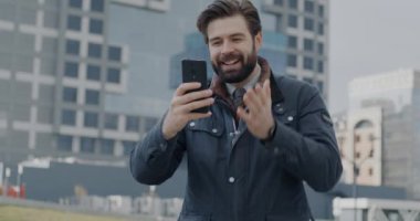 Başarılı bir iş adamı, şehir sokaklarındaki gayrimenkulleri tartışan modern binayı işaret ederek çevrimiçi video görüşmesi yapıyor. İş iletişimi ve sanal buluşma kavramı.
