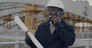 Afrika kökenli Amerikalı mimar, inşaat alanının dışında duran planları cep telefonuyla tartışıyor. Profesyonel iletişim ve insan konsepti.