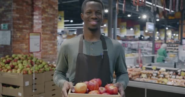 スーパーマーケットの新鮮なりんごの収納箱にエプロンショップアシスタントのアフリカ系アメリカ人のゆっくりとした動きの肖像画 小売業と食料品店のコンセプト — ストック動画