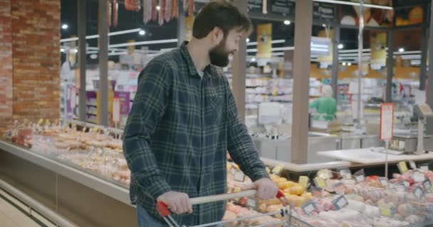 ショッピングのトロリーを持つ若者のゆっくりとした動きは 食べ物を選択し スーパーマーケットでカメラと微笑みに変わります 人と小売店のコンセプト — ストック動画