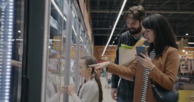 Genç bir aile babası ve çocuk markette akıllı telefon kullanarak yemek satın alıyorlar. Market ve insanlar alışveriş konsepti.