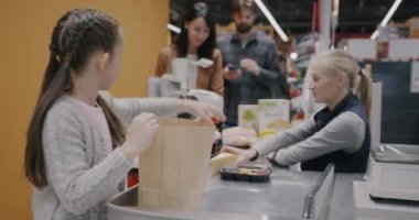 Süpermarkette alışveriş yapan sevimli küçük kız kasiyerle tezgahta kese kağıdı alıyor. Çocukluk ve tüketim kavramı.