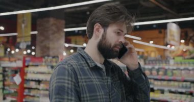 Cep telefonuyla konuşan genç adam perakende mağazasında modern süpermarkette duruyor. Cep telefonu iletişimi ve insan kavramı.