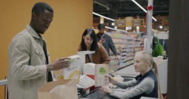 Afrikalı Amerikalı erkek süpermarket müşterisi kasiyerlerin masasından yiyecek paketleme ürünleri alıyor. Perakende işi ve insan konsepti.