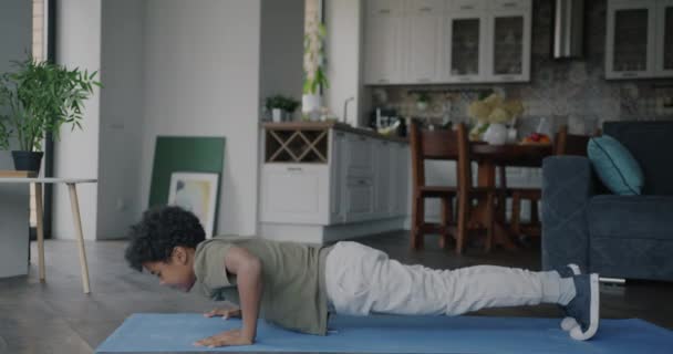 Сильный Маленький Мальчик Занимающийся Спортом Сосредоточен Отжиманиях Тренирующихся Дома Коврике — стоковое видео