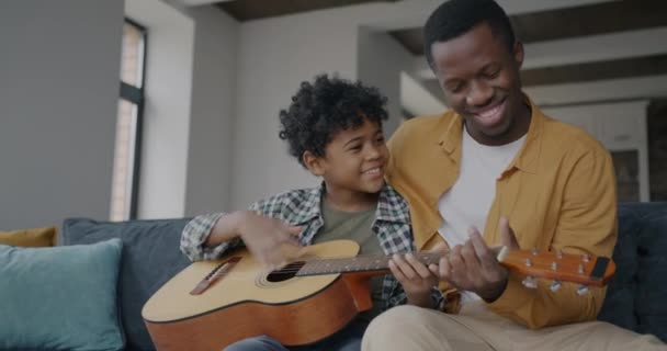 爱爸爸的非裔美国男人教孩子弹吉他 一起在公寓里玩乐 家庭和创造性活动概念 — 图库视频影像