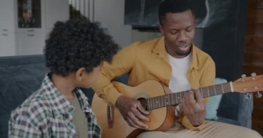 Afrikalı Amerikalı baba gitar çalıyor ve oğluyla birlikte şarkı söylüyor evde boş zamanların tadını çıkarıyor. Yaratıcı gençlik ve aile ilişkileri kavramı.